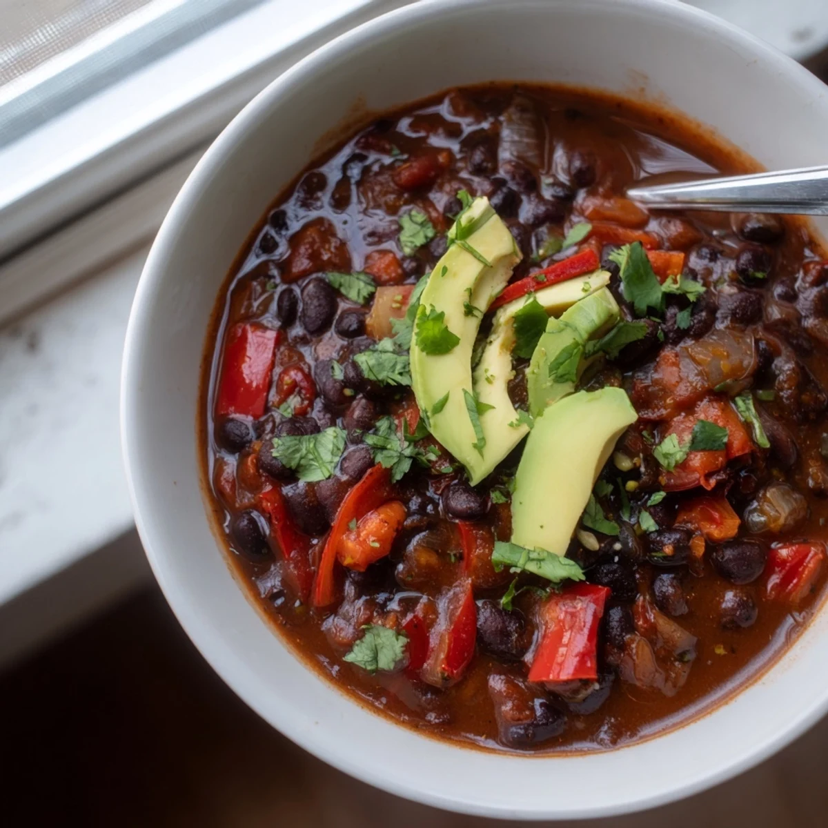 Vibrant Spicy Black Bean Chili garnished with fresh cilantro and lime wedges.  