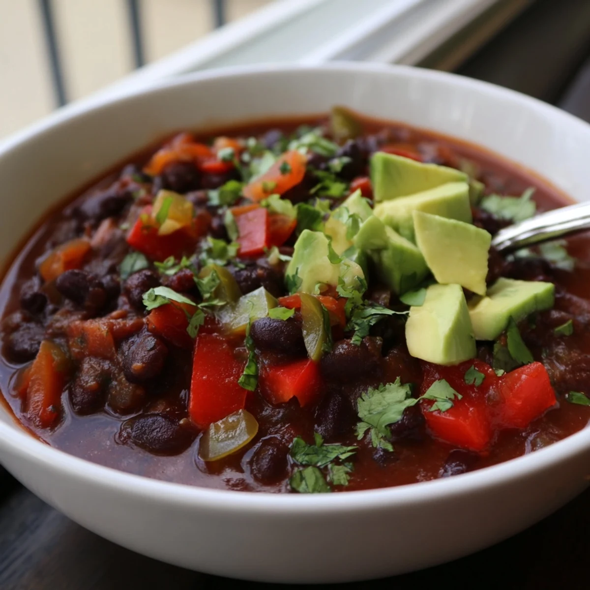 A steaming bowl of Spicy Black Bean Chili topped with creamy avocado slices.  