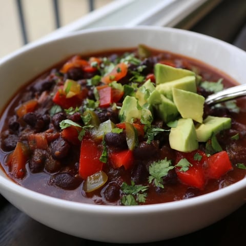 A steaming bowl of Spicy Black Bean Chili topped with creamy avocado slices.  