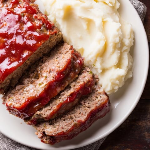 Steaming hot Classic Meatloaf & Mashed Potatoes, glazed and ready to serve with fluffy, creamy mashed potatoes.