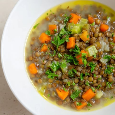Steaming bowl filled with Lentil Soup with Carrots and Celery, garnished with fresh herbs.