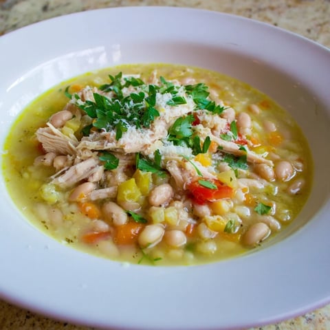Close-up of a steaming bowl of White Bean and Roasted Red Pepper Chicken, garnished with fresh parsley.