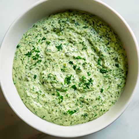 Creamy, vibrant Green Goddess Dip swirled in a bowl, alongside colorful vegetable sticks for dipping pleasure.