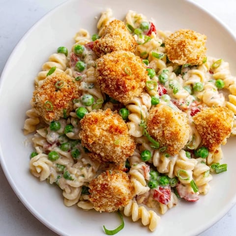 A close-up of crispy chicken bites tossed in creamy ranch dressing with rotini pasta, sweet peas, and diced red bell pepper in a serving bowl.