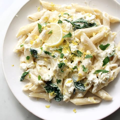A close-up of creamy feta spinach pasta with wilted greens and crumbled cheese in a skillet, steam rising.  