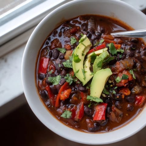 Vibrant Spicy Black Bean Chili garnished with fresh cilantro and lime wedges.  