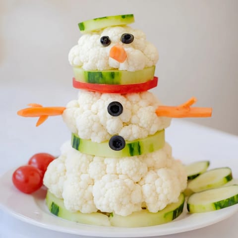 Festive snowman Crudités assembled with carrot scarves, olive eyes, and a flavorful Greek yogurt dip.