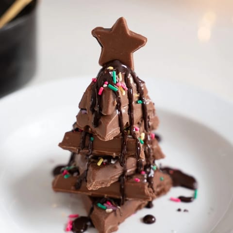 Melted chocolate drizzled over festive Chocolate Kinder Christmas Trees, topped with edible stars.