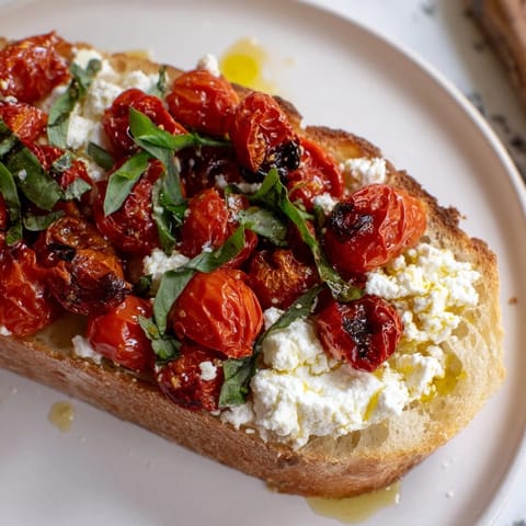 Savory Baked Feta Toast with warm, creamy feta and blistered tomatoes on crunchy bread, drizzled with olive oil and fresh oregano.