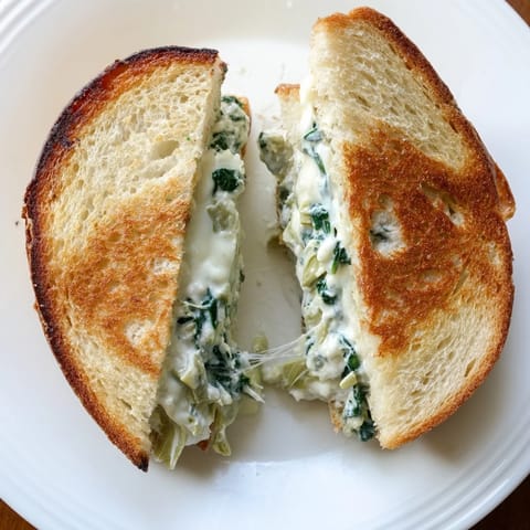 A close-up view of Spinach Artichoke Grilled Cheese, featuring melted mozzarella and chopped artichokes oozing from crispy buttery bread.