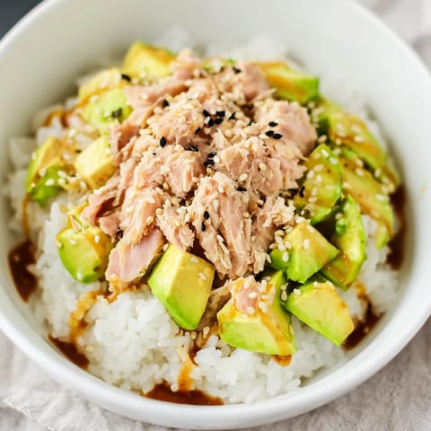 A close-up of the vibrant Tuna Avocado Rice Bowl highlights drizzled ginger-soy dressing and fresh scallions.  