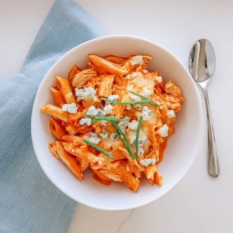 A close-up of Buffalo Chicken Pasta in a skillet, featuring shredded chicken and creamy orange sauce.  