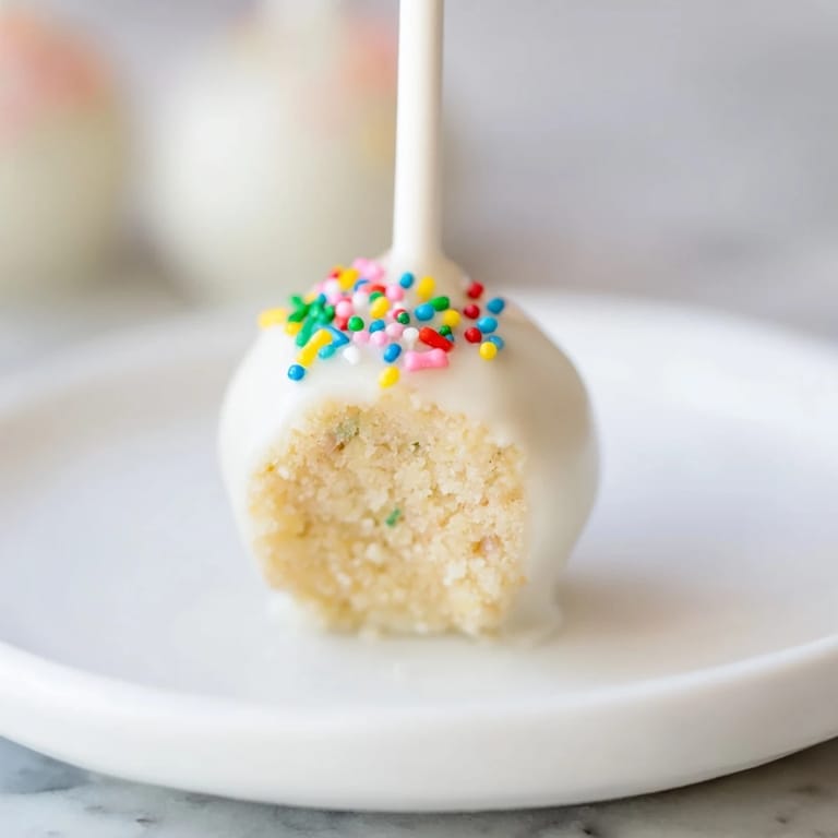 These Lightened-Up Sugar Cookie Cake Pops are coated in white chocolate with colorful sprinkles, a perfect indulgence.