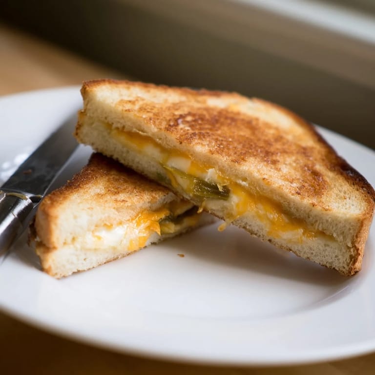 The Cheddar Jalapeño Grilled Cheese sits on a rustic wooden board next to a bowl of creamy tomato soup, perfect for a comforting lunch.