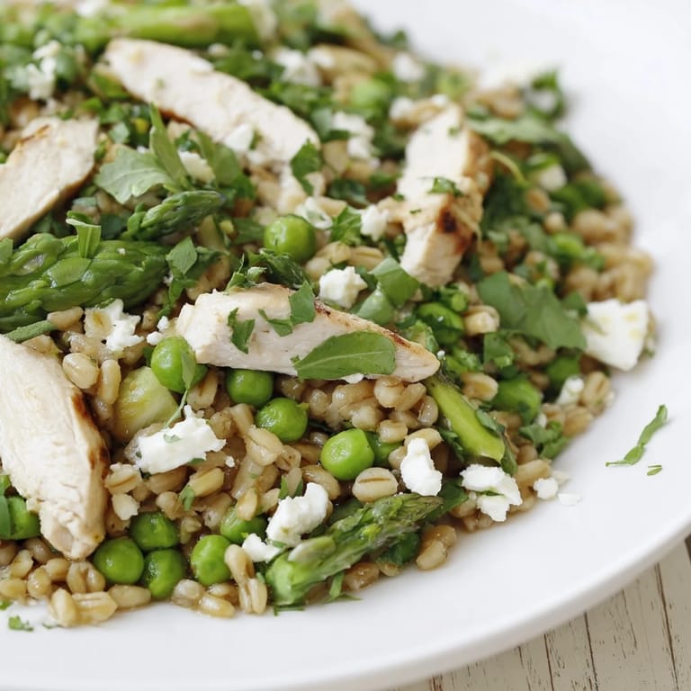 A vibrant bowl of farro chicken salad features feta and fresh herbs, perfect for a spring dinner.