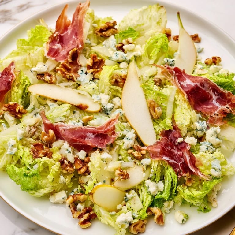 Enjoy Frisée, Pear, Blue Cheese, and Crispy Prosciutto Salad as a light lunch, featuring toasted walnuts and a tangy vinaigrette.