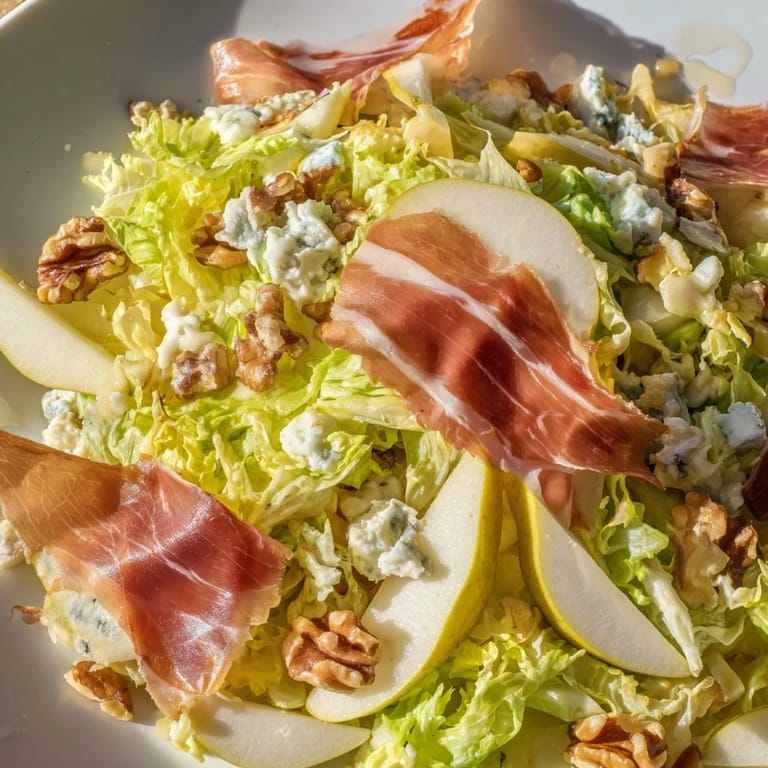 Frisée, Pear, Blue Cheese, and Crispy Prosciutto Salad tossed with creamy blue cheese crumbles and fresh, crisp frisée on a white plate.