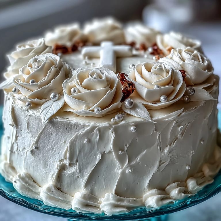 Tender vanilla sponge layered with silky buttercream and crowned with delicate white roses and a cross topper.